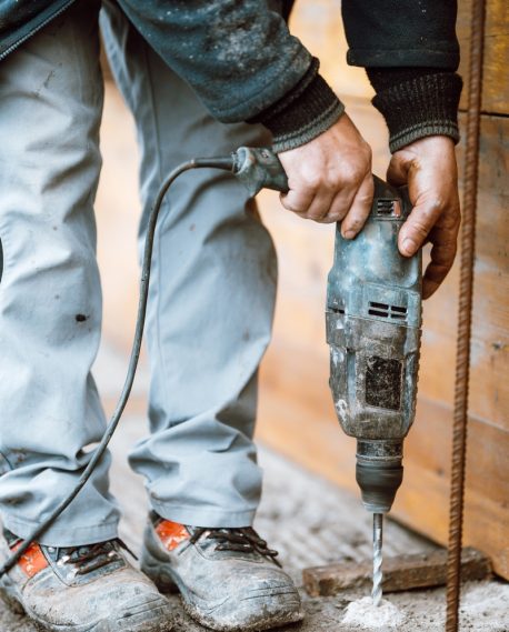 Builder working with rotary hammer drill perforator equipment making holes in concrete on construction site Builder working with rotary hammer drill perforator equipment making holes in concrete on construction site